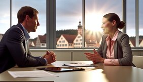 Zwei Fachleute im Gespräch an einem Besprechungstisch mit Blick auf eine deutsche Stadtlandschaft